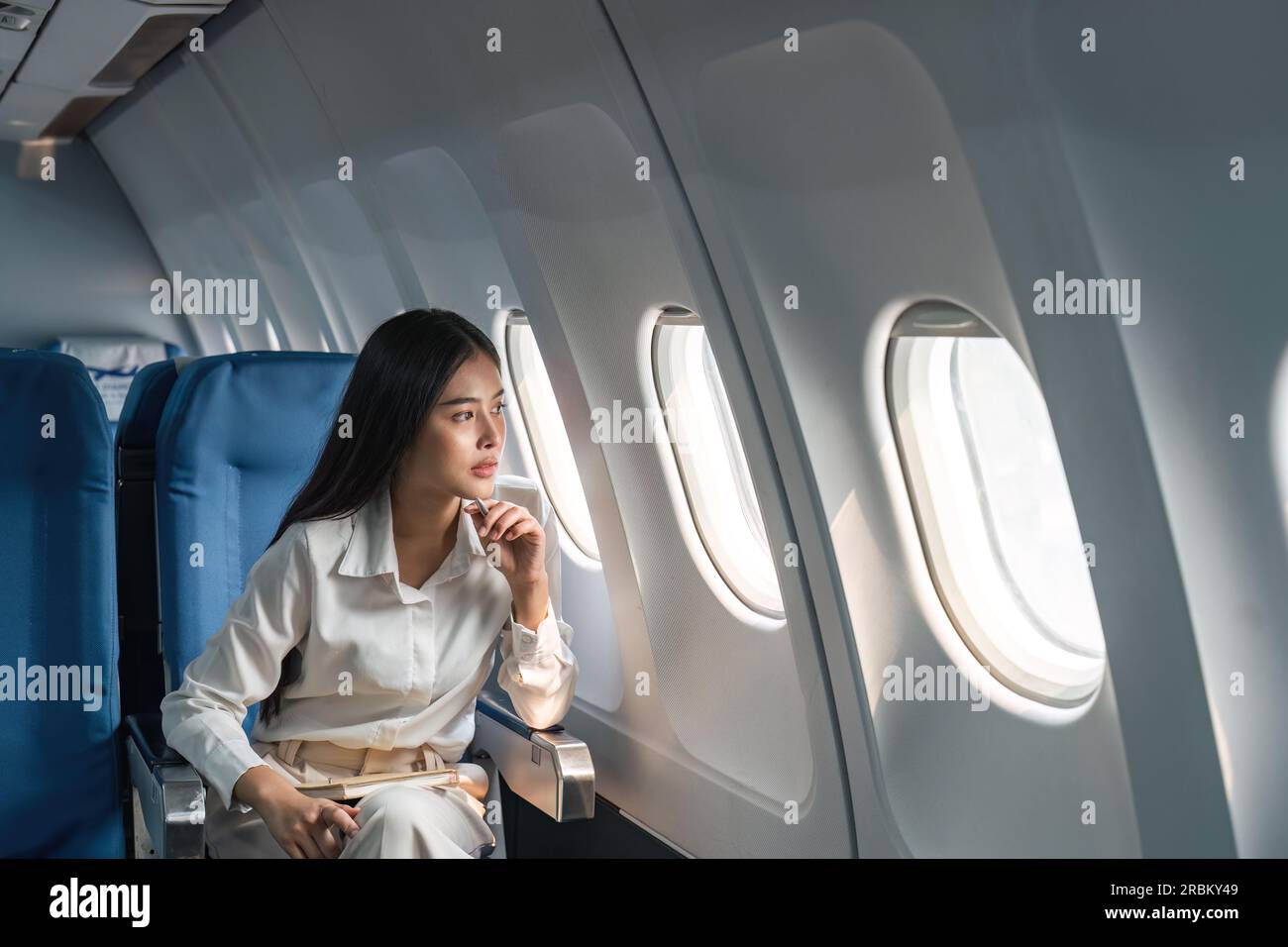 Asian woman passenger sitting in airplane near window and looking out the window Stock Photo