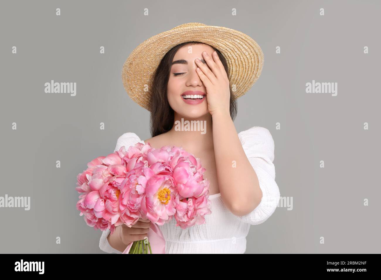 Beautiful young woman in straw hat with bouquet of pink peonies against ...