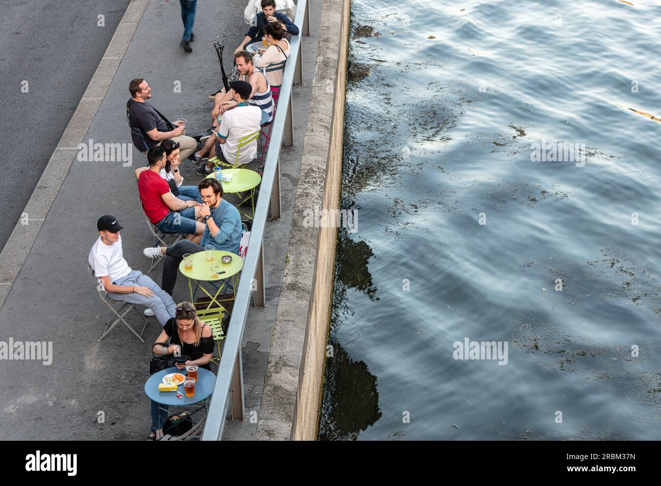 People eat, drink and socialise on the River Seine riverside on Right Bank on Voie Georges Pompidou opposite Ile Saint-Louis. Paris. Stock Photo
