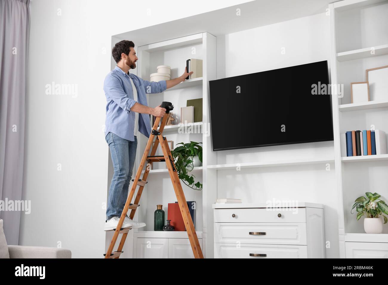 Man on wooden folding ladder taking book from shelf at home Stock Photo ...