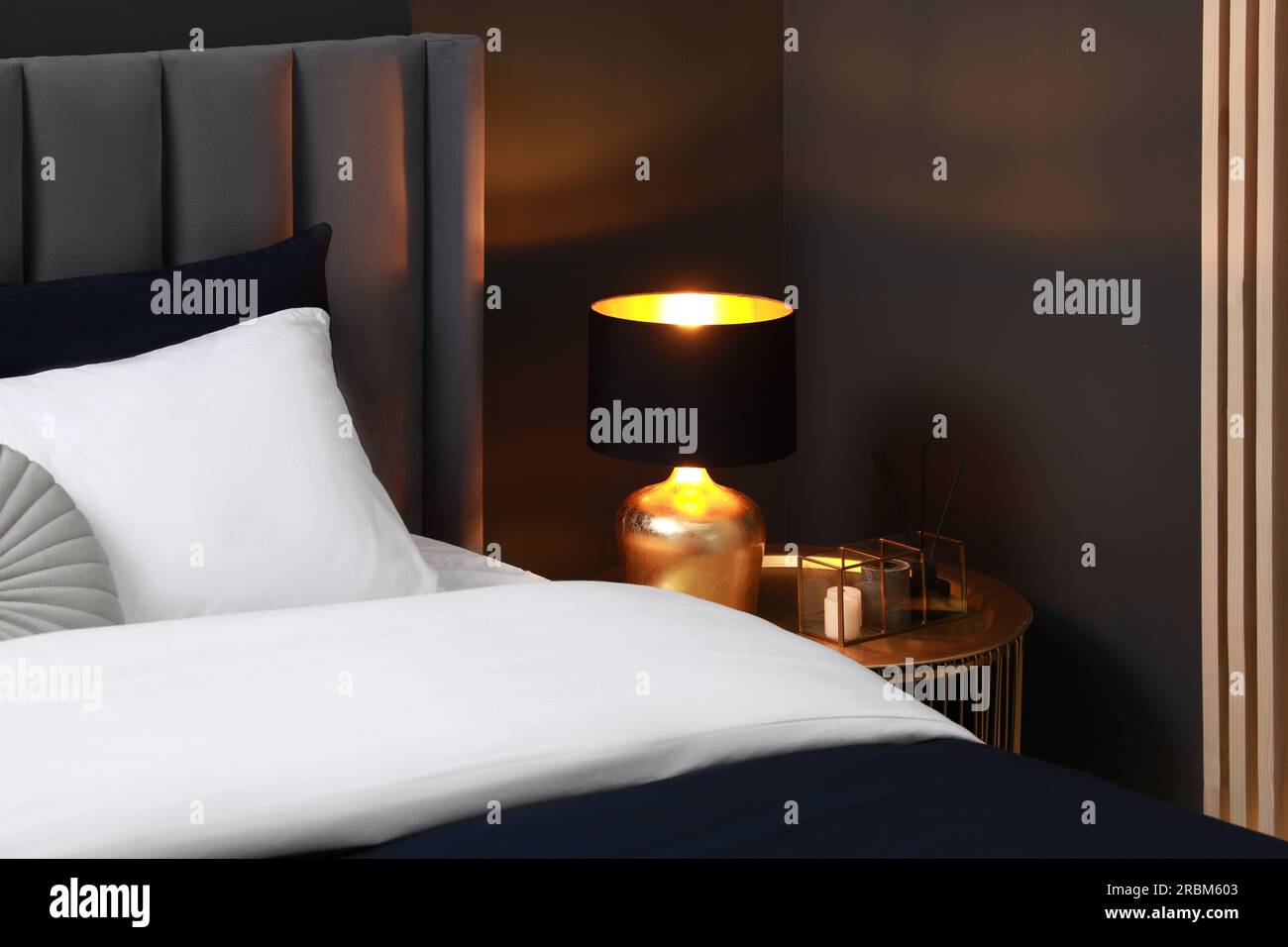 Comfortable bed with cushions, lamp and different decor on bedside table in room. Stylish interior Stock Photo