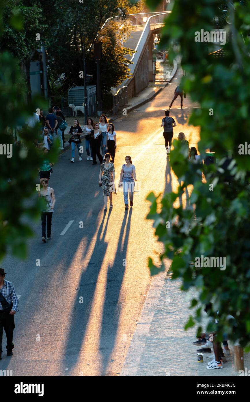 People promenade at sunset with long shadows and silouettes on River Seine Right Bank on Voie Georges Pompidou opposite Ile Saint-Louis. Paris. Stock Photo
