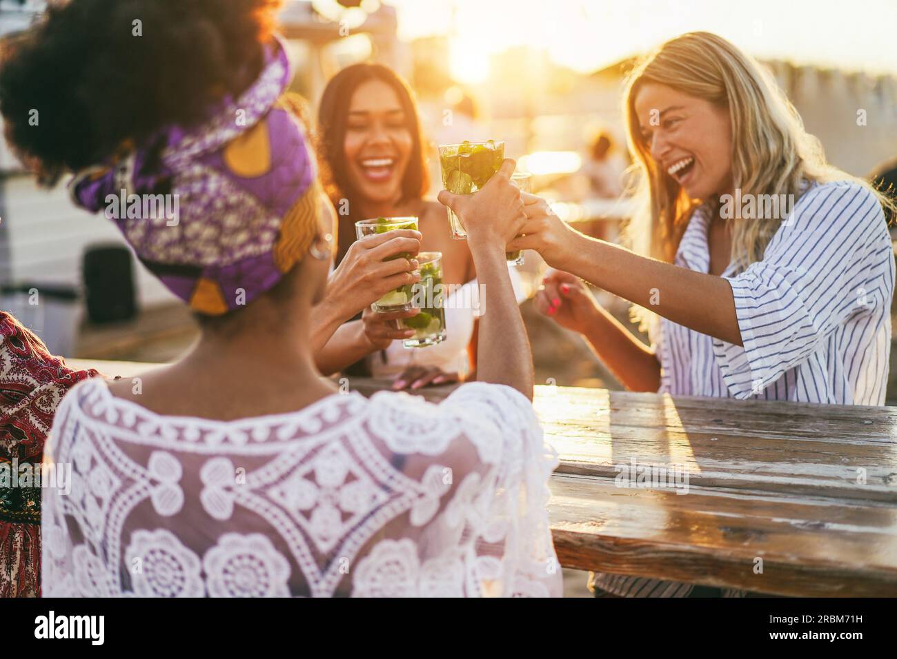 Multiracial happy friends cheering and drinking mojitos at beach party - Focus on center hand holding cocktail Stock Photo