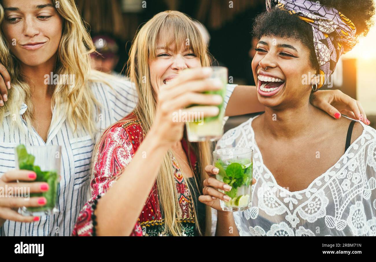 Multiracial girls having fun dancing and drinking with cocktails at bar on the beach - Soft focus on african girl face Stock Photo