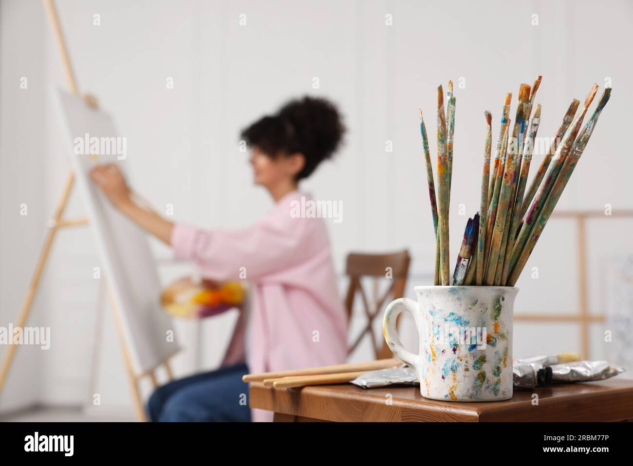 Young woman painting on easel with canvas in studio, focus on brushes ...