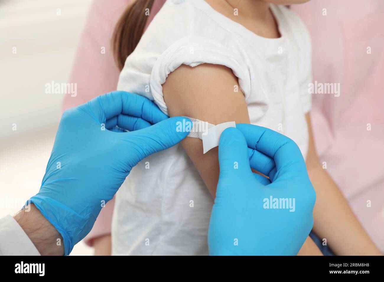 Children's hepatitis vaccination. Mother with her daughter. Doctor sticking medical plaster on little girl's arm, closeup Stock Photo