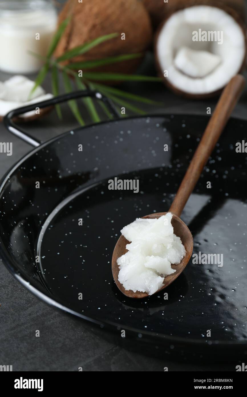 Frying pan with organic coconut cooking oil and wooden spoon on grey ...