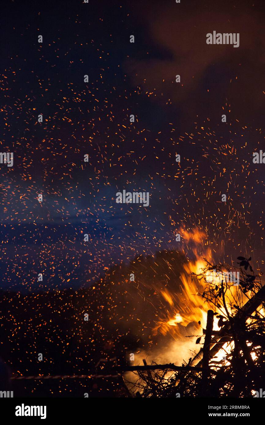 Sparks and embers fly from  a bonfire, creating tiny points of light against the night sky. Stock Photo