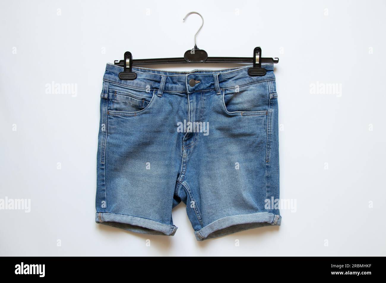 Denim men's shorts on a hanger on a white background, fashionable clothes Stock Photo
