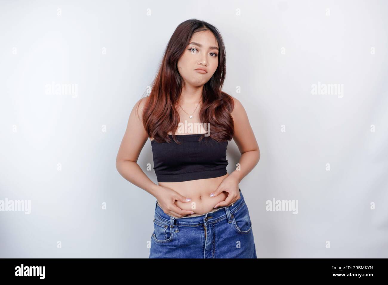 A sad young Asian woman pinching flabby skin fat belly isolated by white background Stock Photo