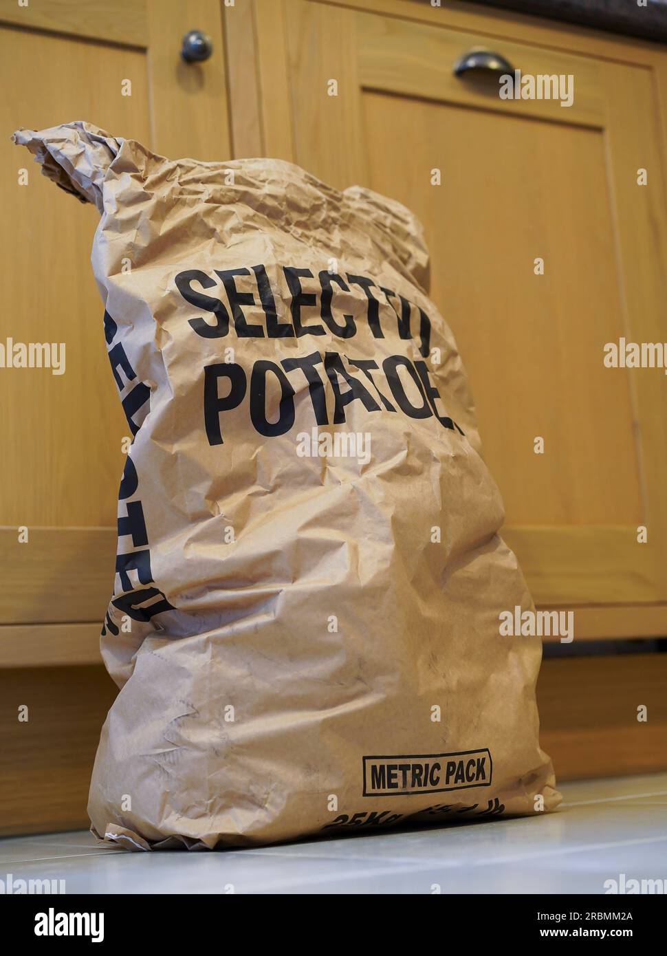 25kg brown paper sack of potatoes/ sack of spuds standing on the floor in a UK kitchen. Stock Photo