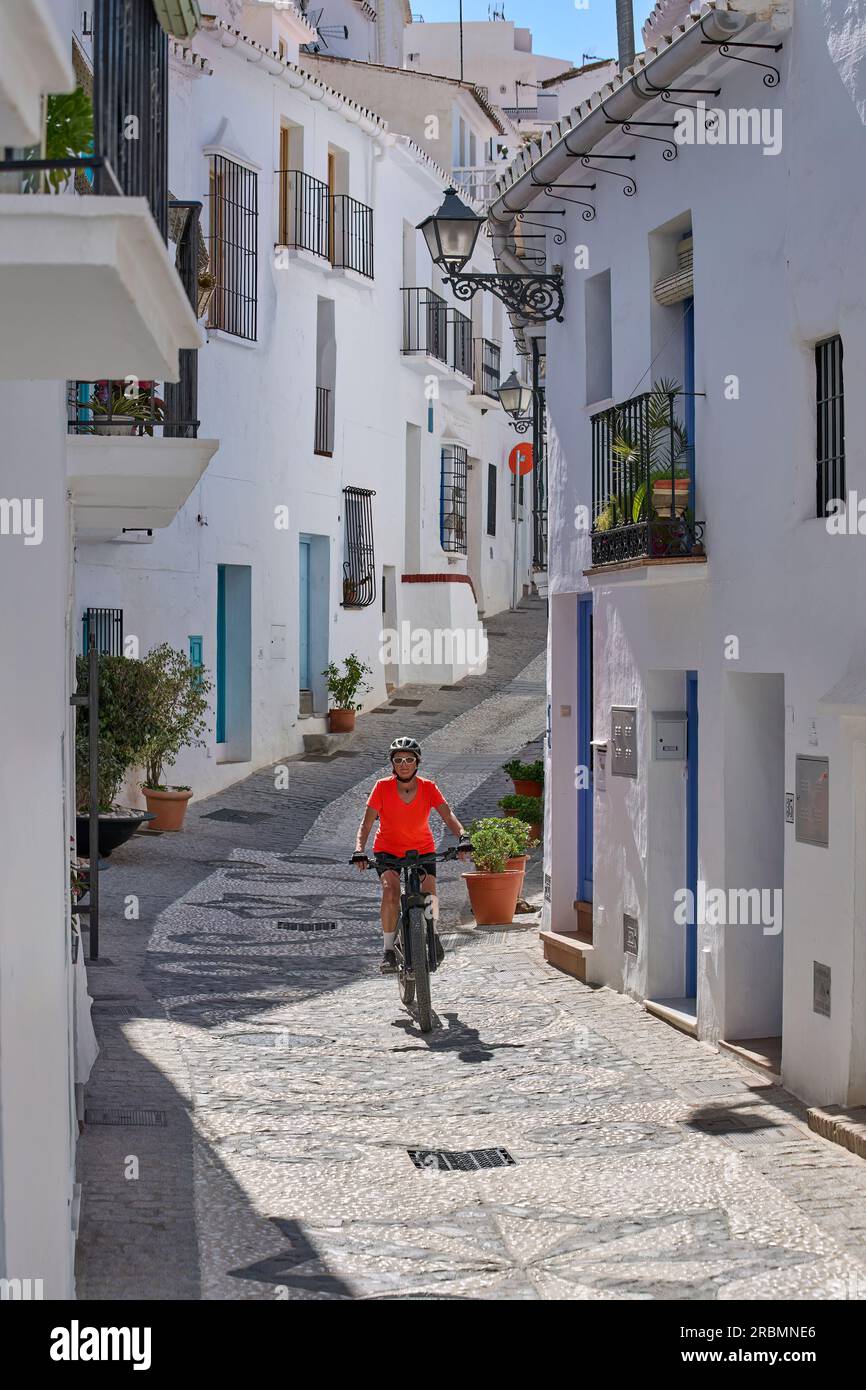nice senior woman cycling with her electric mountain bike in the picturesque white village of Frigiliana near Nerja, Andalusia, Spain Stock Photo