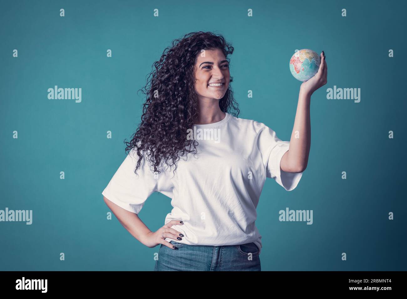 Studio shot of beautiful confident caucasian curly model woman wears blue jeans and casual basic solid white t-shirt, isolated over blue background. P Stock Photo