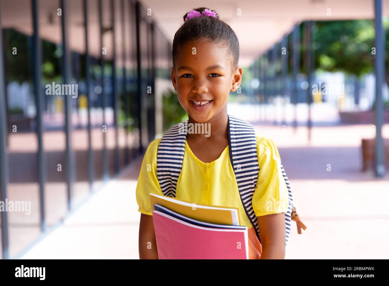 Happy biracial schoolgirl with school bag holding books, smiling