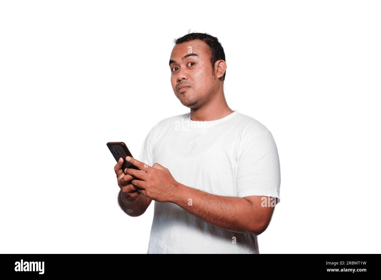 Excited Asian man wearing white Tshirt smiling while holding his phone, isolated by white background Stock Photo