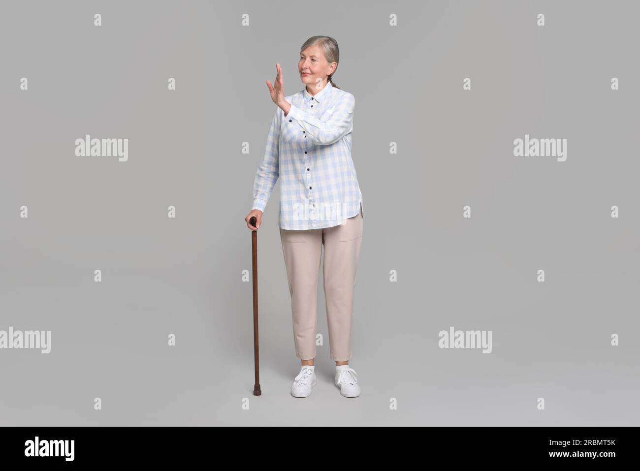 Senior woman with walking cane waving on gray background Stock Photo ...