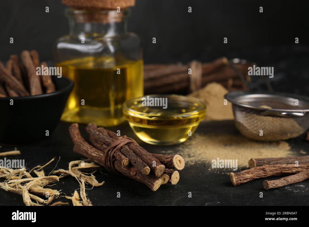 Dried sticks of licorice roots, powder and essential oil on black table