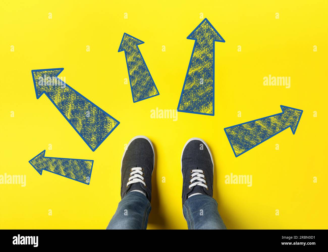 Choosing future profession. Teenager standing in front of drawn signs on yellow background, top view. Arrows pointing in different directions symboliz Stock Photo
