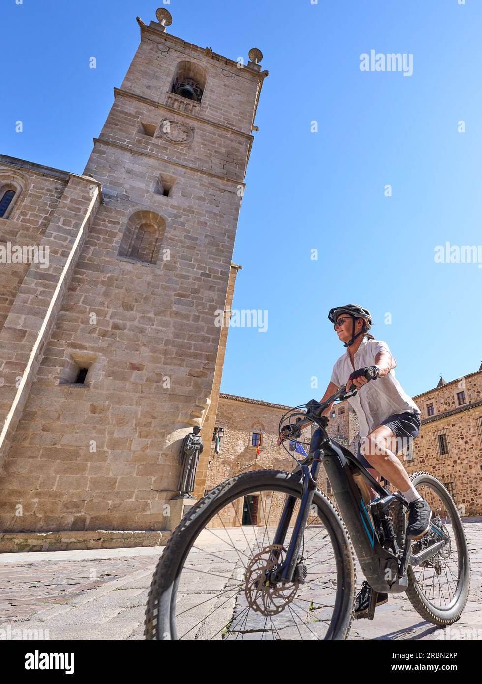 cheerful senior woman cycling with her electric mountain bike in the medieaval and moorish downtown of Caceres, Extremadura, Spain Stock Photo