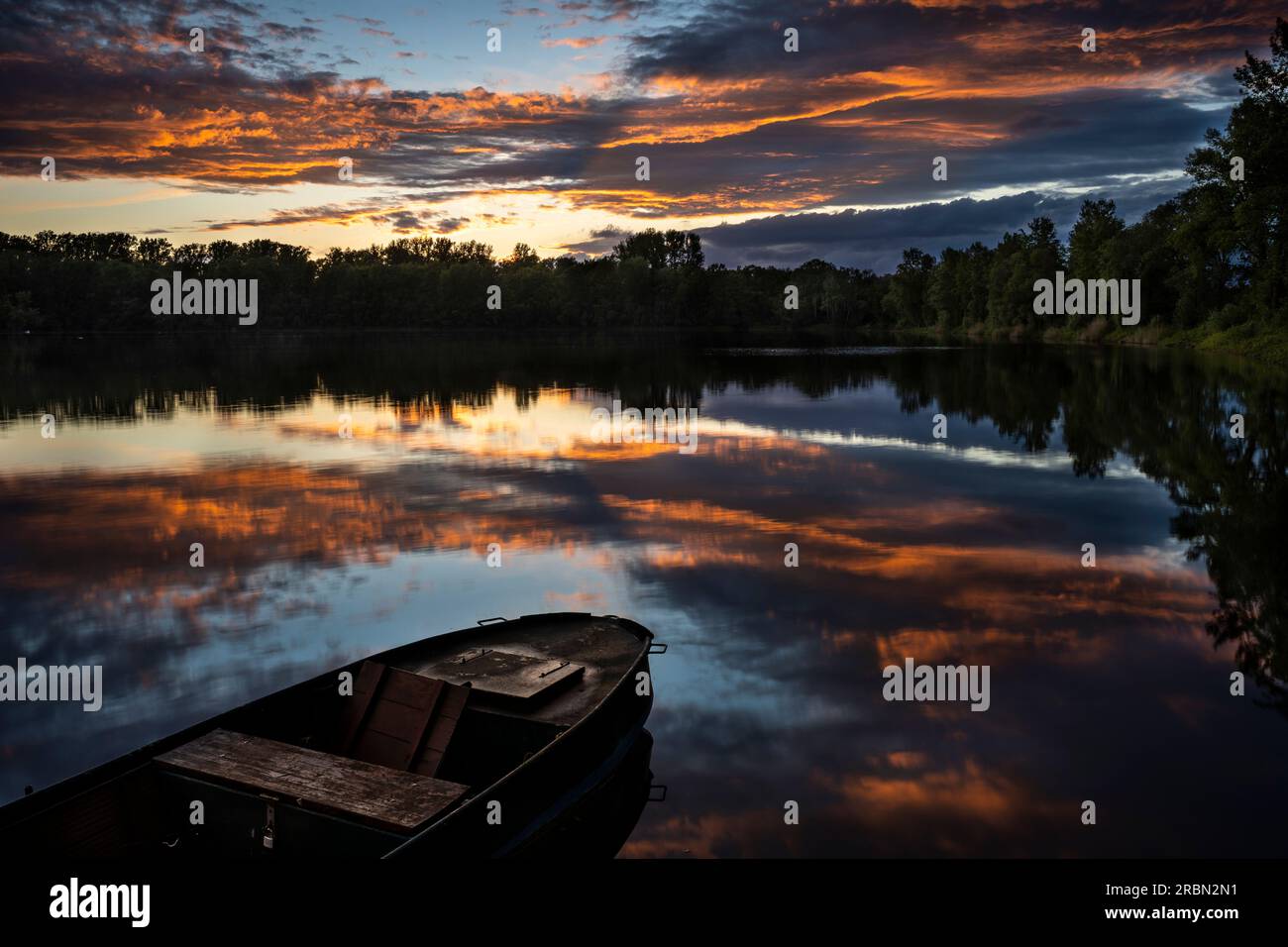 A lake at sunset, a boat in front. Orange clouds in the sky, reflecting in the lake. Rhine-Neckar-Region, Germany. Stock Photo