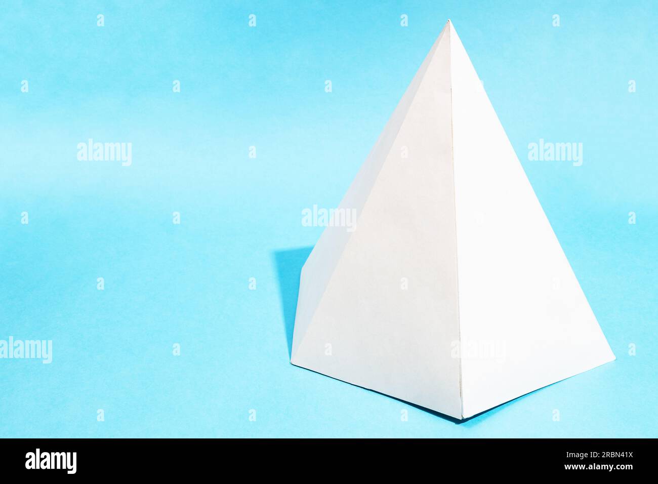 handcrafted paper hexagonal pyramid on turquoise blue background with copyspace Stock Photo