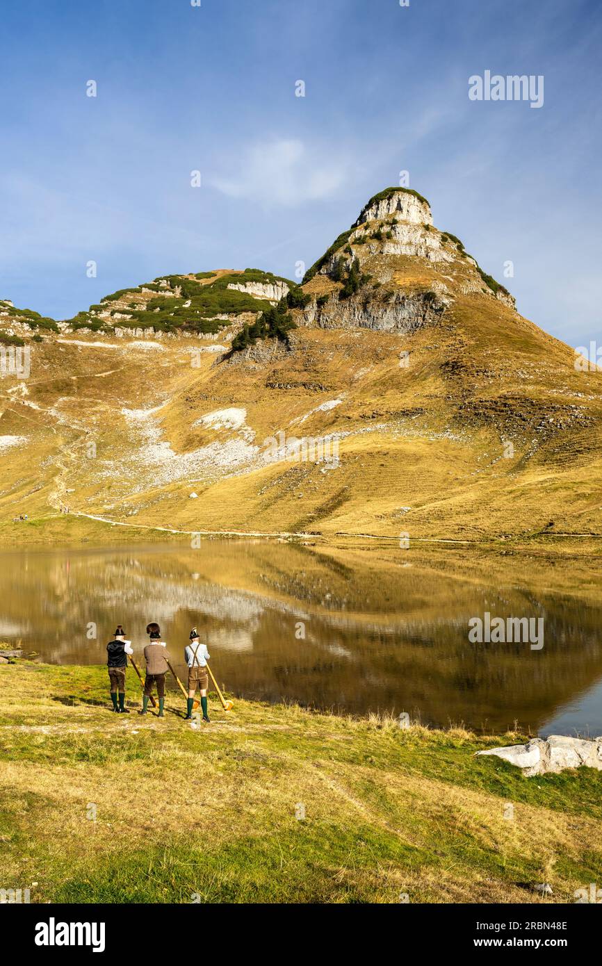 Three Austrian alphorn musicians named 'Klangholz' playing alphorn at lake Augstsee on mount Loser in Austria. Stock Photo