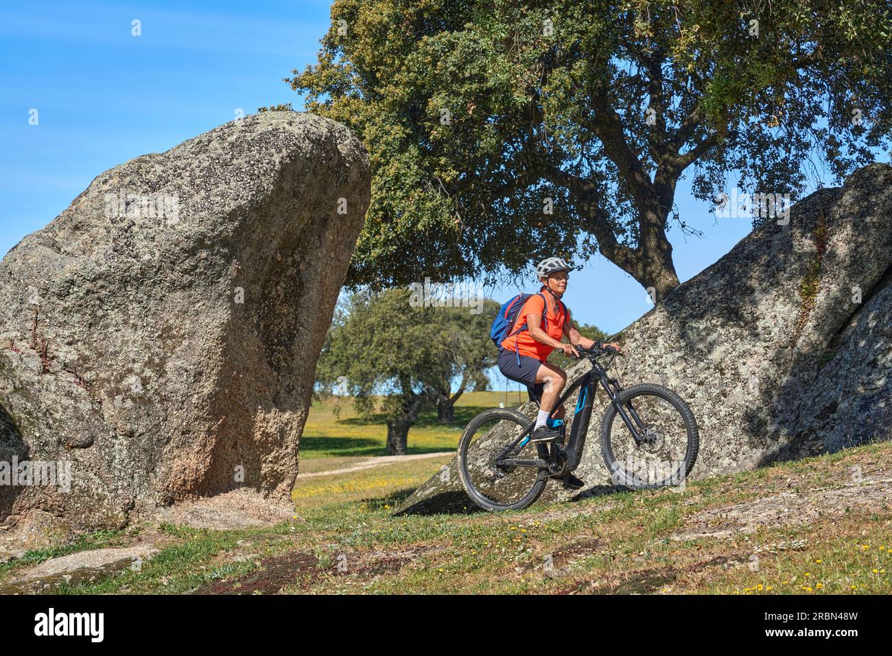 nice senior woman cyling with her electric mountain bike in a stone oak forest of the Extremadura department of Spain Stock Photo