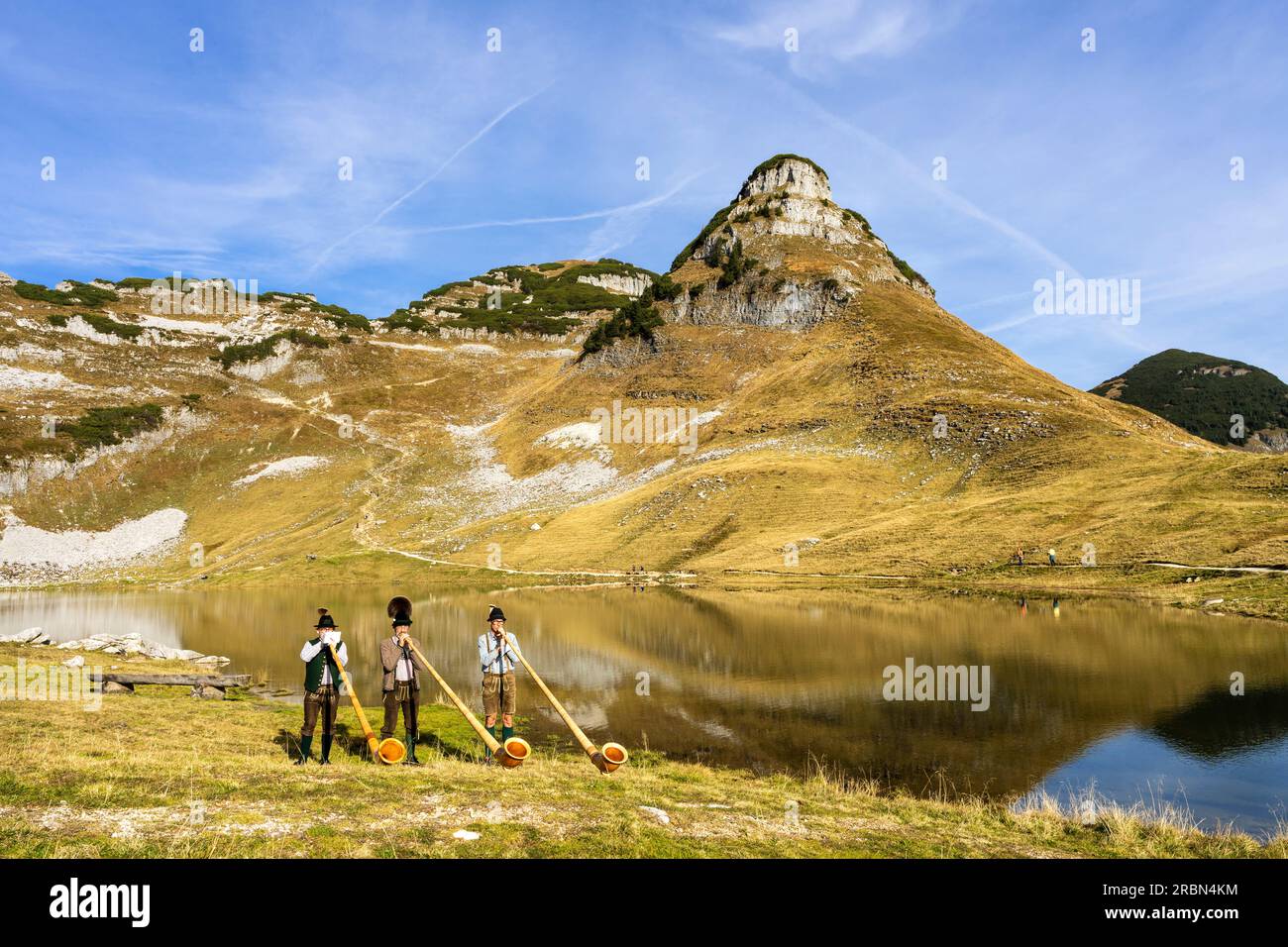 Three Austrian alphorn musicians named "Klangholz" playing alphorn at lake Augstsee on mount Loser in Austria. Stock Photo