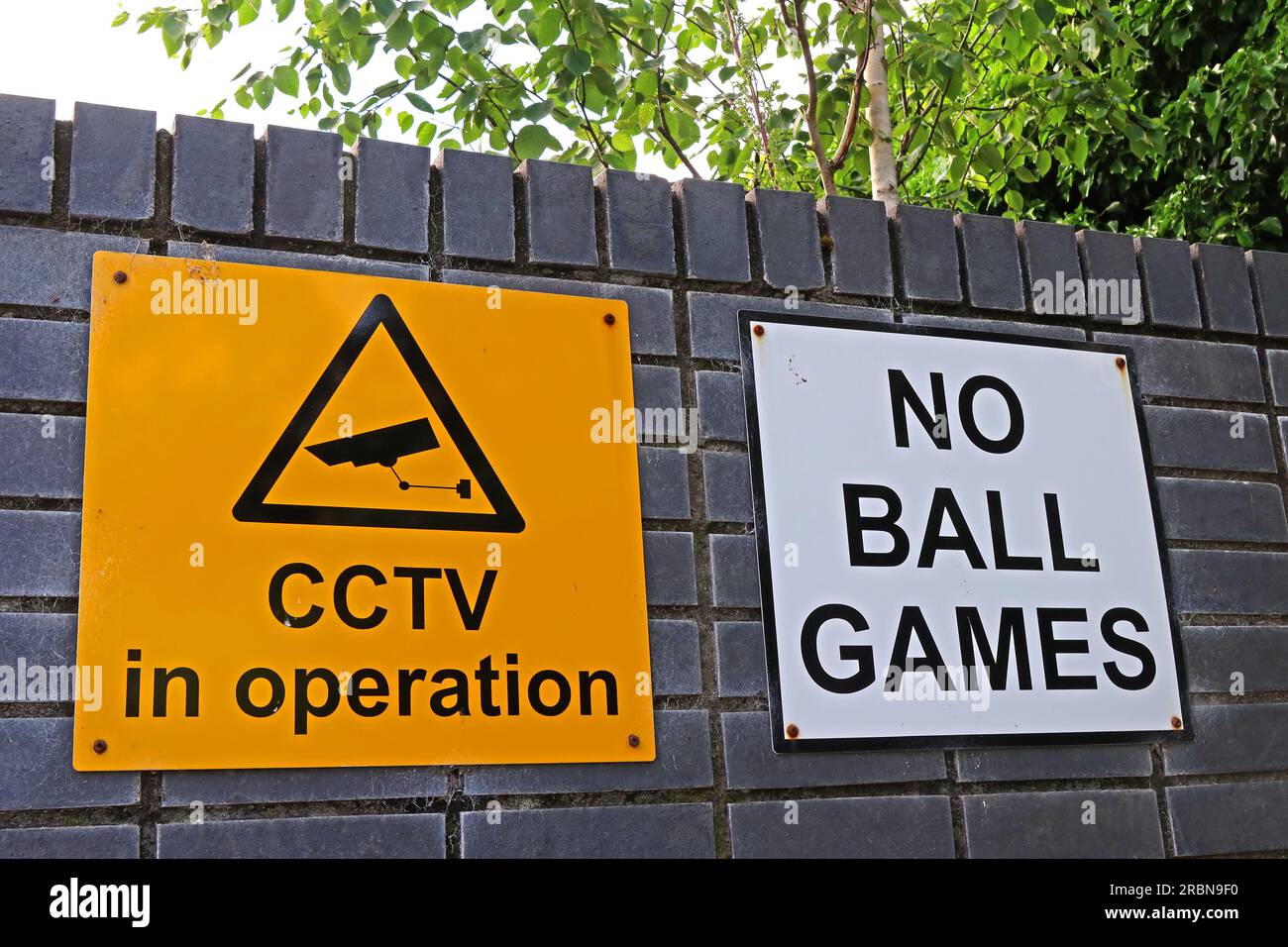CCTV in operation and “No ball games” signs mounted on a high wall on a UK council housing estate, highlighting surveillance, estate rules, and ASB Stock Photo
