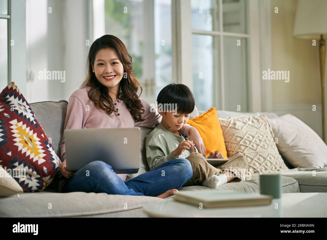 beautiful asian mother and five-year-old son sitting on family couch at home looking at camera smiling Stock Photo
