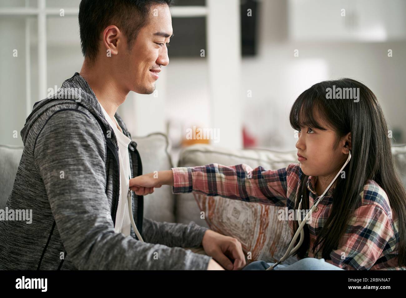 young asian father playing doctor and patient game with seven-year-old daughter at home Stock Photo
