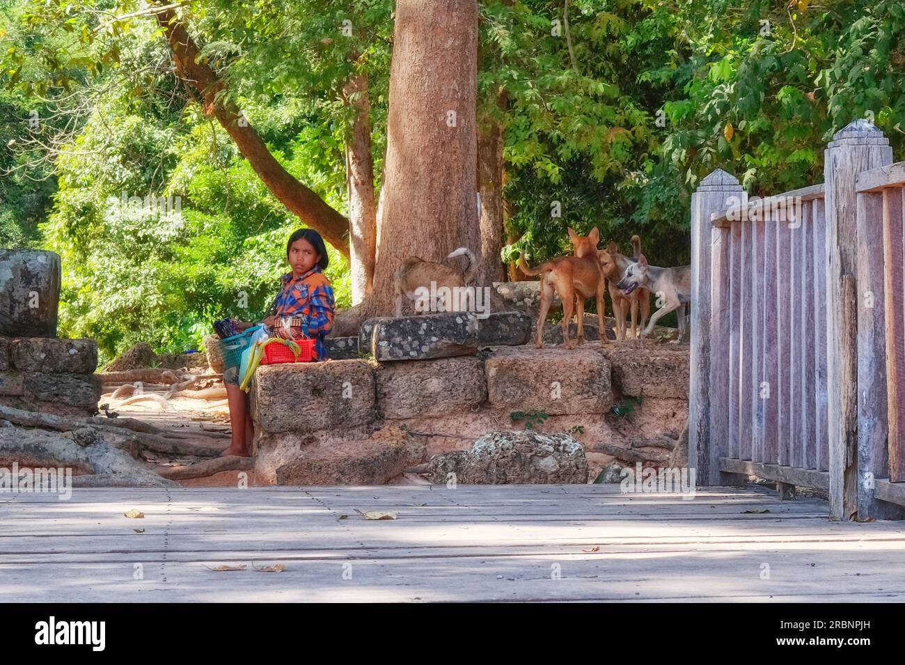 Siem Reap, Cambodia, December 19, 2018. A young Khmer girl sits on ancient stone blocks and sells souvenirs. Stock Photo