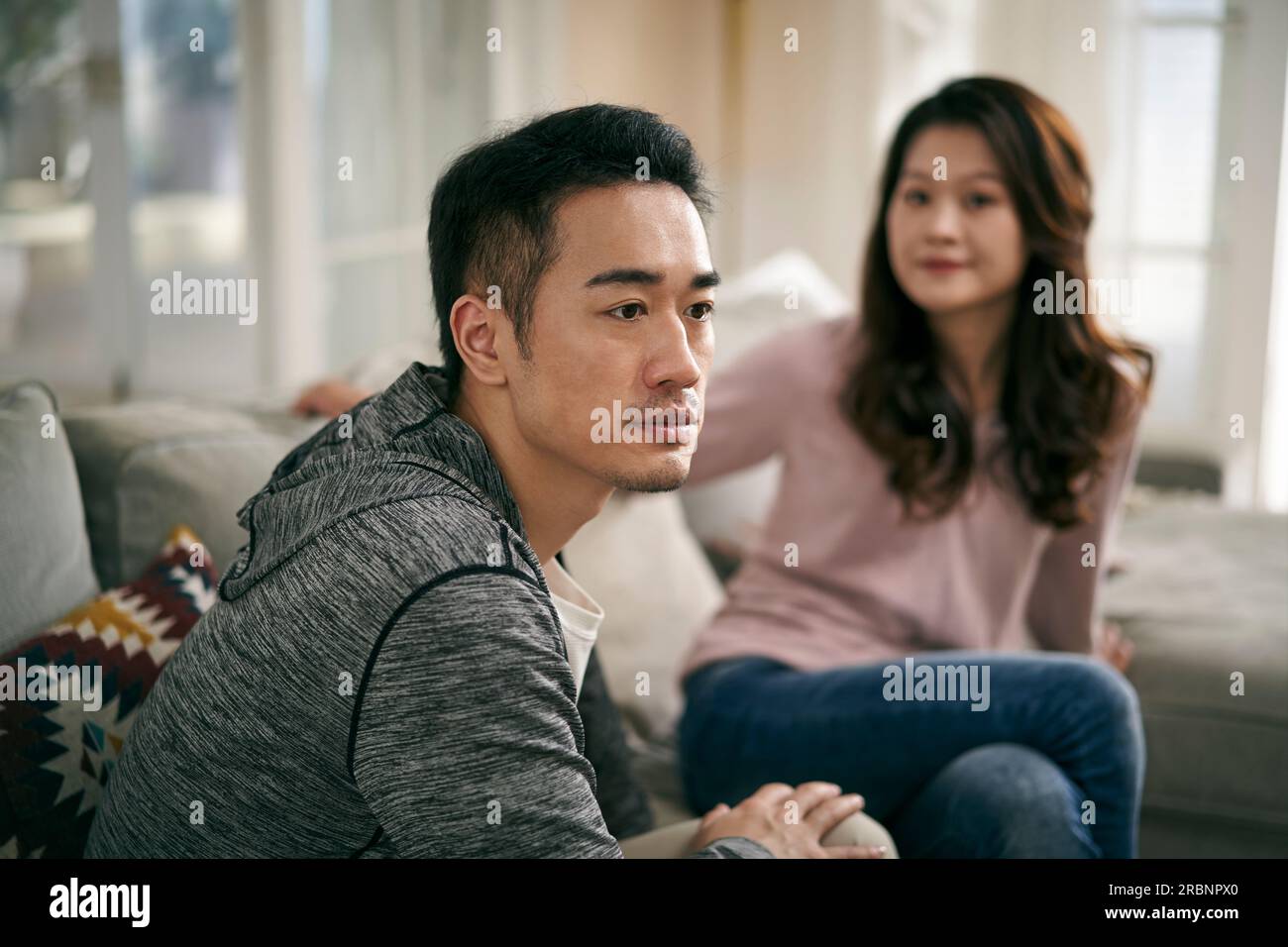 young asian couple sitting on family couch at home talking through their marriage problems Stock Photo