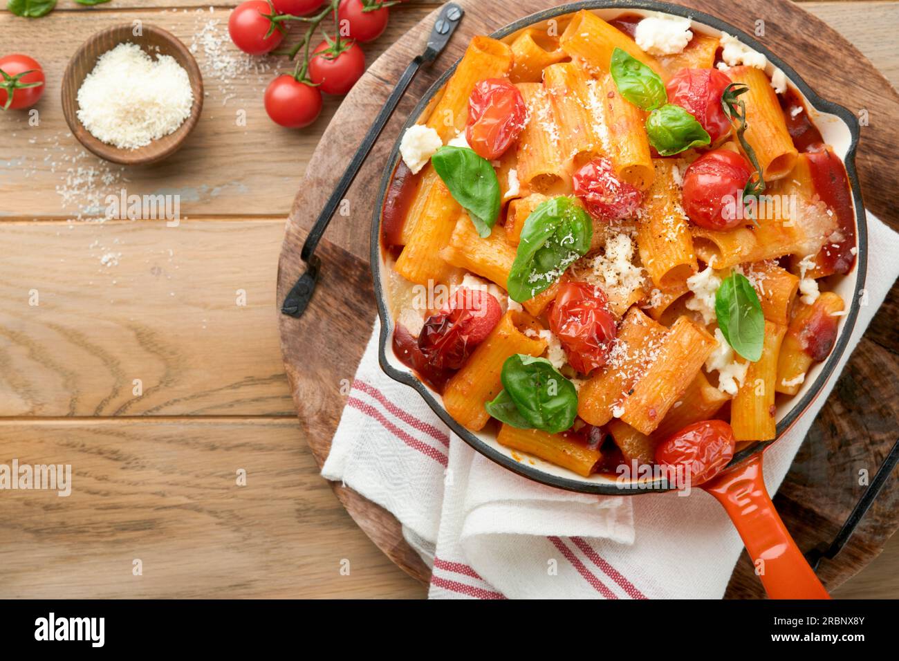Pasta Tortiglioni with tomato sauce, baked cherry tomatoes, mozzarella and parmesan cheese, basil on old rustic table background. Traditional Italian Stock Photo