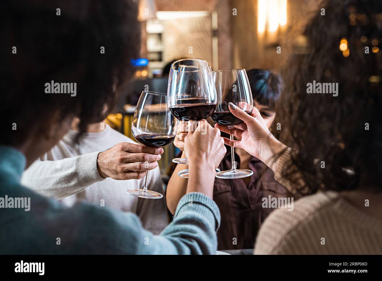 Multicultural friends raise wine glasses for a toast in an elegant restaurant. Viewed from outside through a window, the focus is on the glasses. Stock Photo