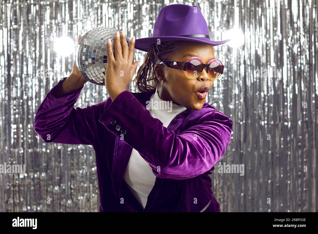 Happy black woman holding glitter ball and dancing to music at funky nightclub disco party Stock Photo