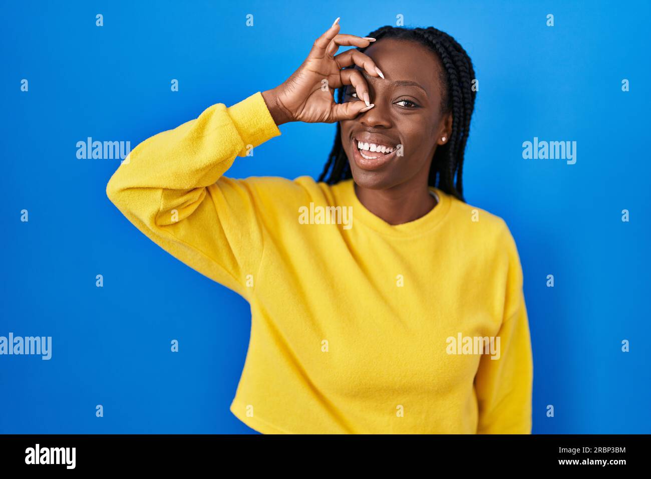 Beautiful black woman standing over blue background doing ok gesture ...