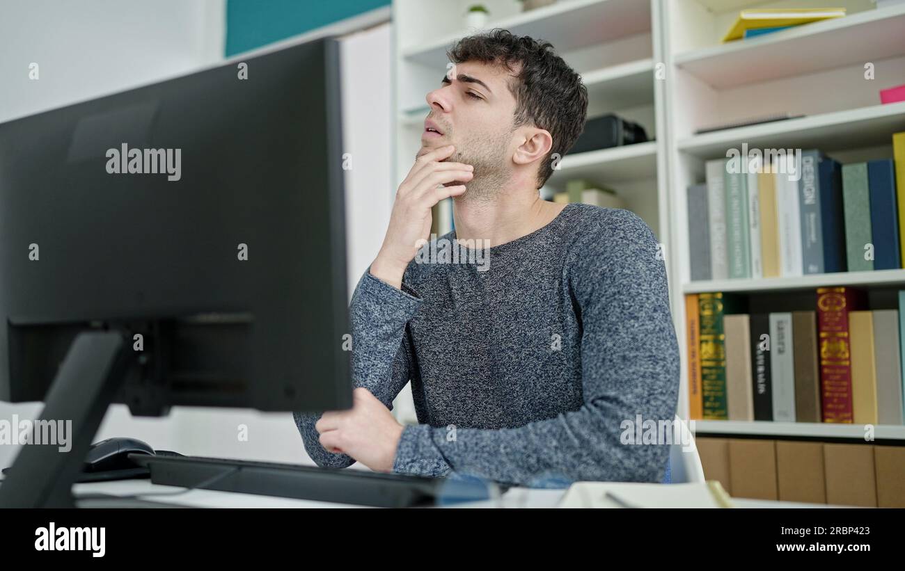 Young hispanic man using computer thinking at library university Stock Photo
