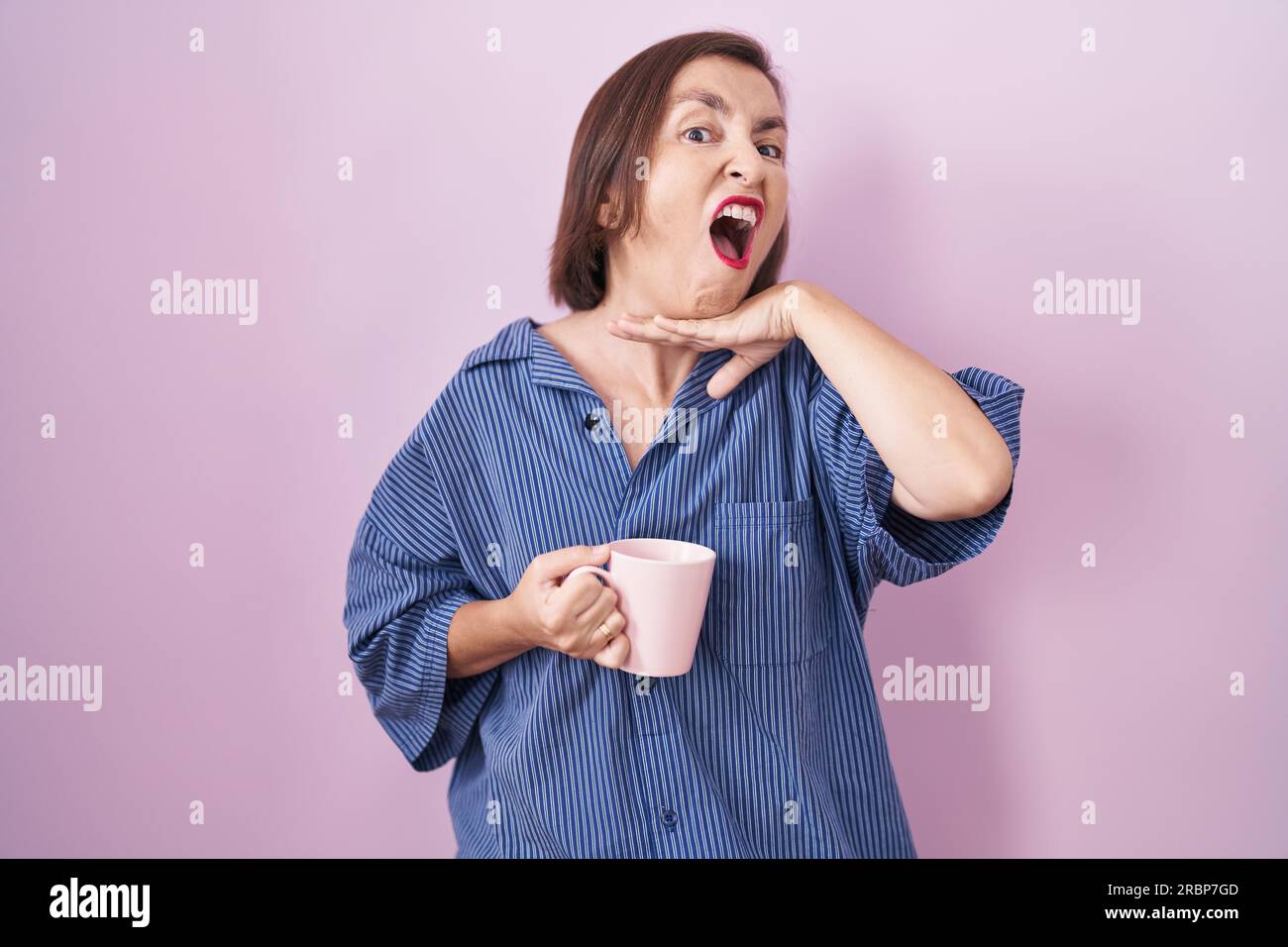 Middle age hispanic woman drinking a cup coffee cutting throat with hand as knife, threaten aggression with furious violence Stock Photo