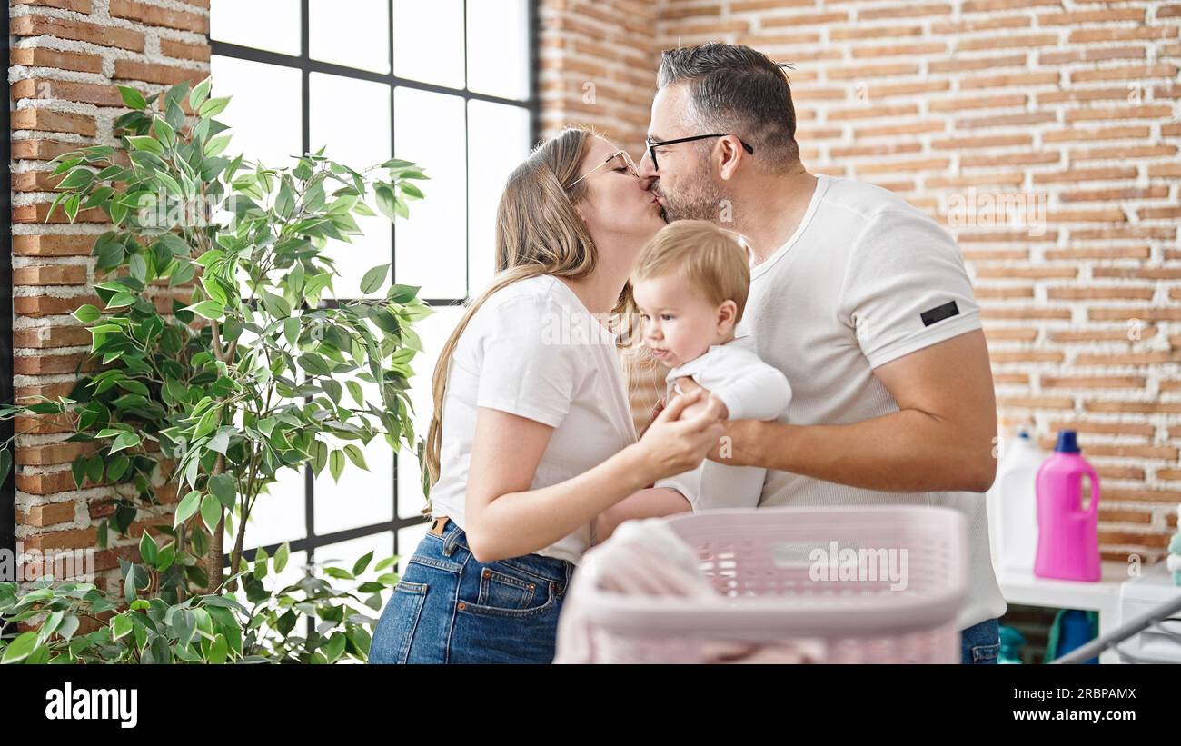Family of mother, father and baby doing laundry kissing at laundry room Stock Photo