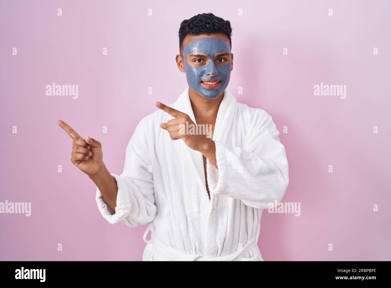 Young hispanic man wearing beauty face mask and bath robe smiling and ...