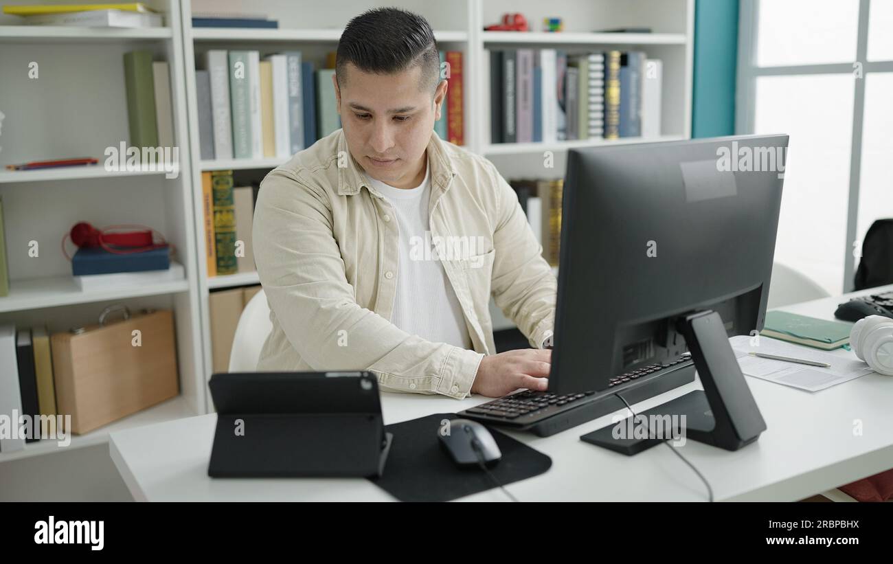 Young hispanic man student using computer and touchpad studying at ...