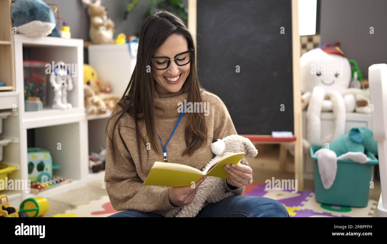 Beautiful hispanic woman preschool teacher reading story book sitting