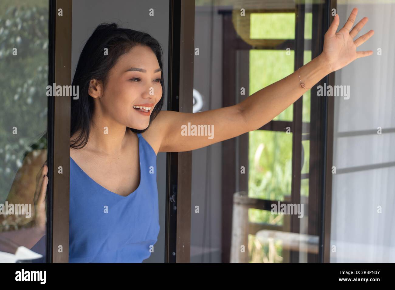 Cheerful woman waving hand from open window Stock Photo