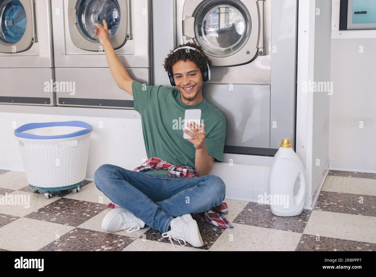 Guy Using Phone Listening Music While Doing Laundry At Laundromat Stock Photo