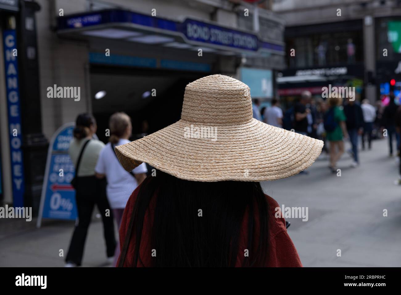 Woman wearing straw summer hat walking long Oxford Street past Bond Street Underground Station, central London, England, UK Stock Photo