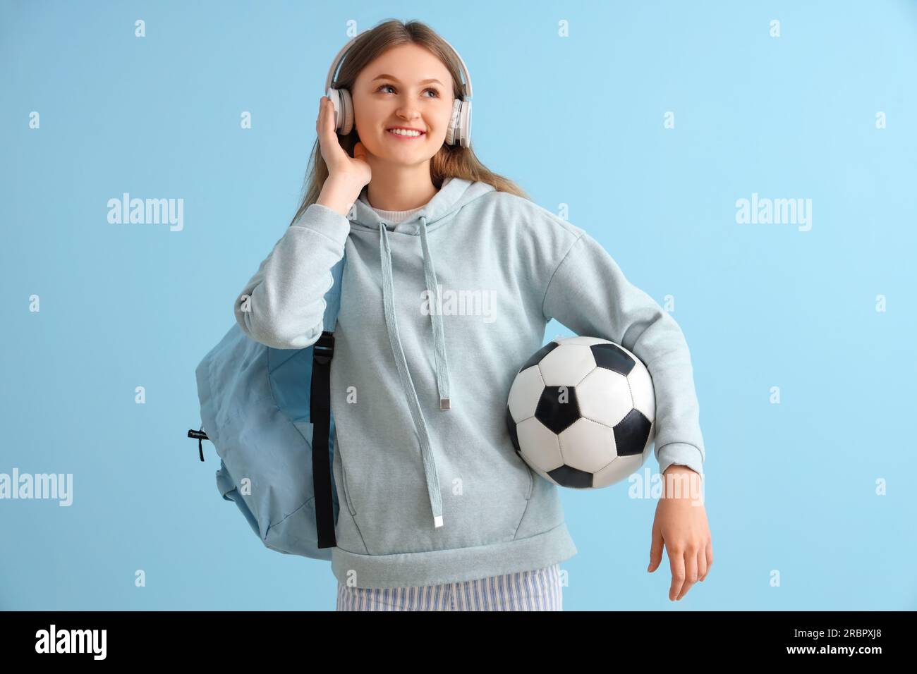 Female student with backpack and soccer ball listening music in ...