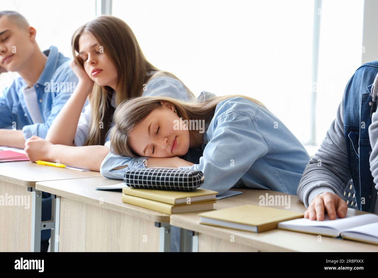 Tired sleepy classmates sitting at desks in classroom Stock Photo