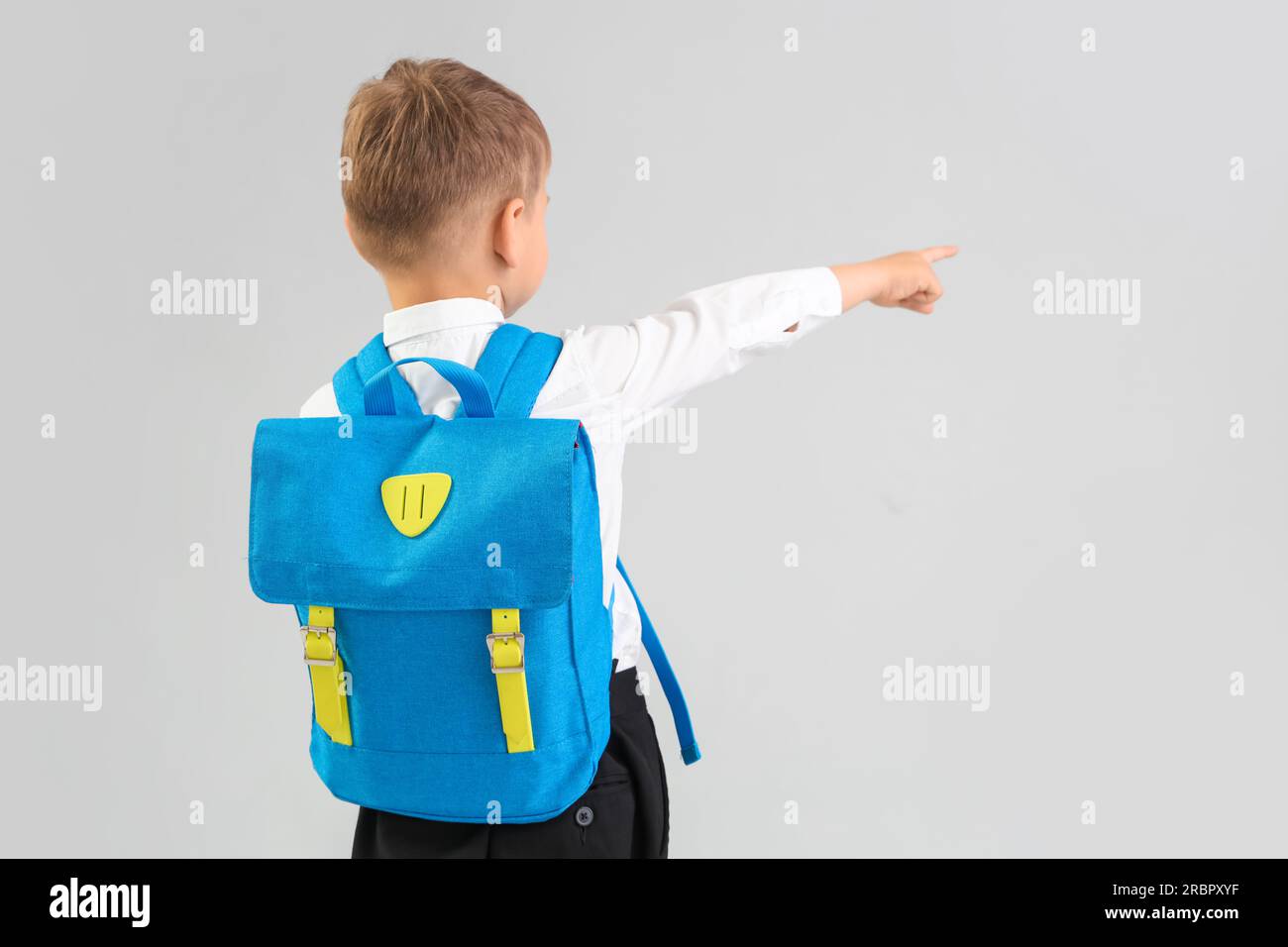 Little schoolboy with blue backpack pointing at something on grey ...