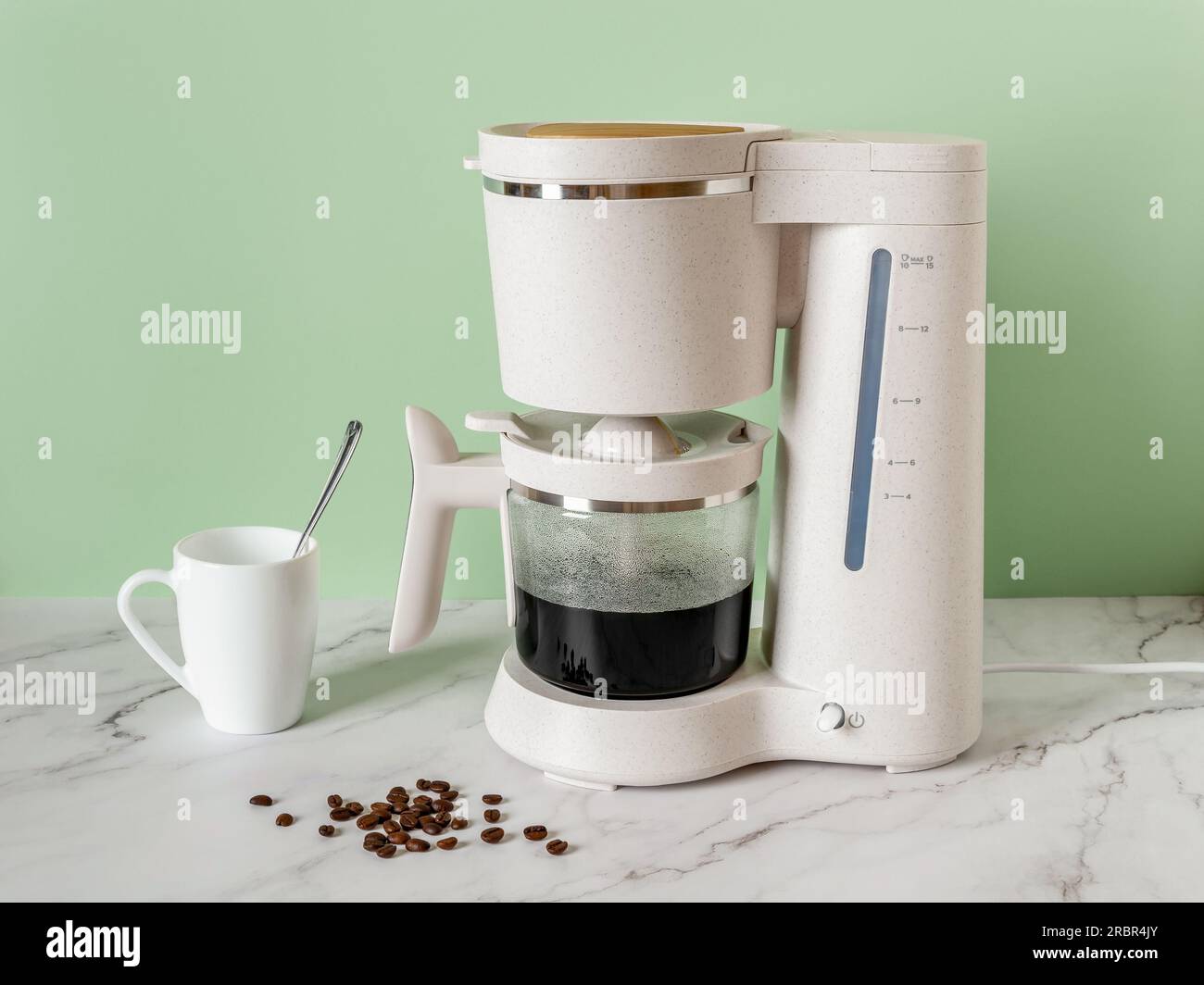 Automatic drip coffee maker brews a morning drink. Electric coffee machine filling glass pot with hot black coffee on a marble countertop at home. Stock Photo